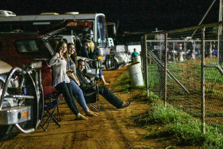 Spectators leaning against cars watching the sprint car race