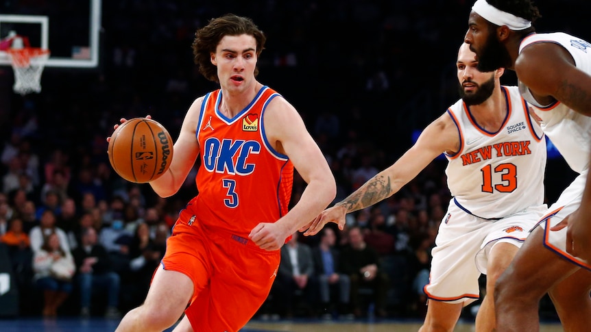 Oklahoma City NBA player Josh Giddey dribbles the basketball around New York Knicks defenders.
