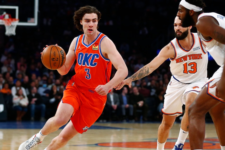 Oklahoma City NBA player Josh Giddey dribbles the basketball around New York Knicks defenders.