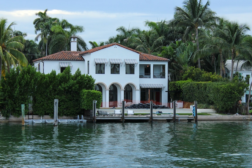 A big white house sits right near the water with palm trees behind it