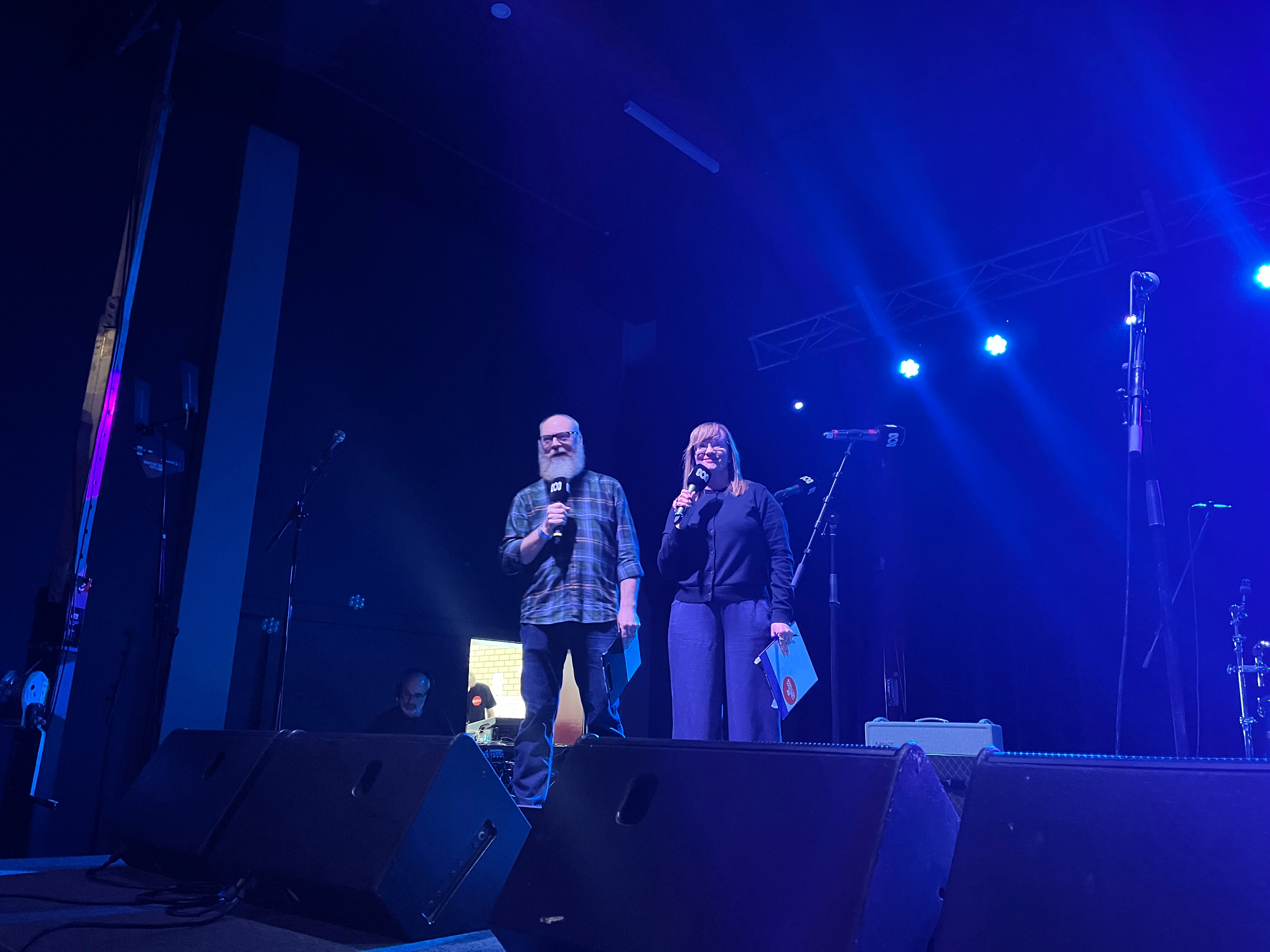 A man and a woman stand on stage holding microphones