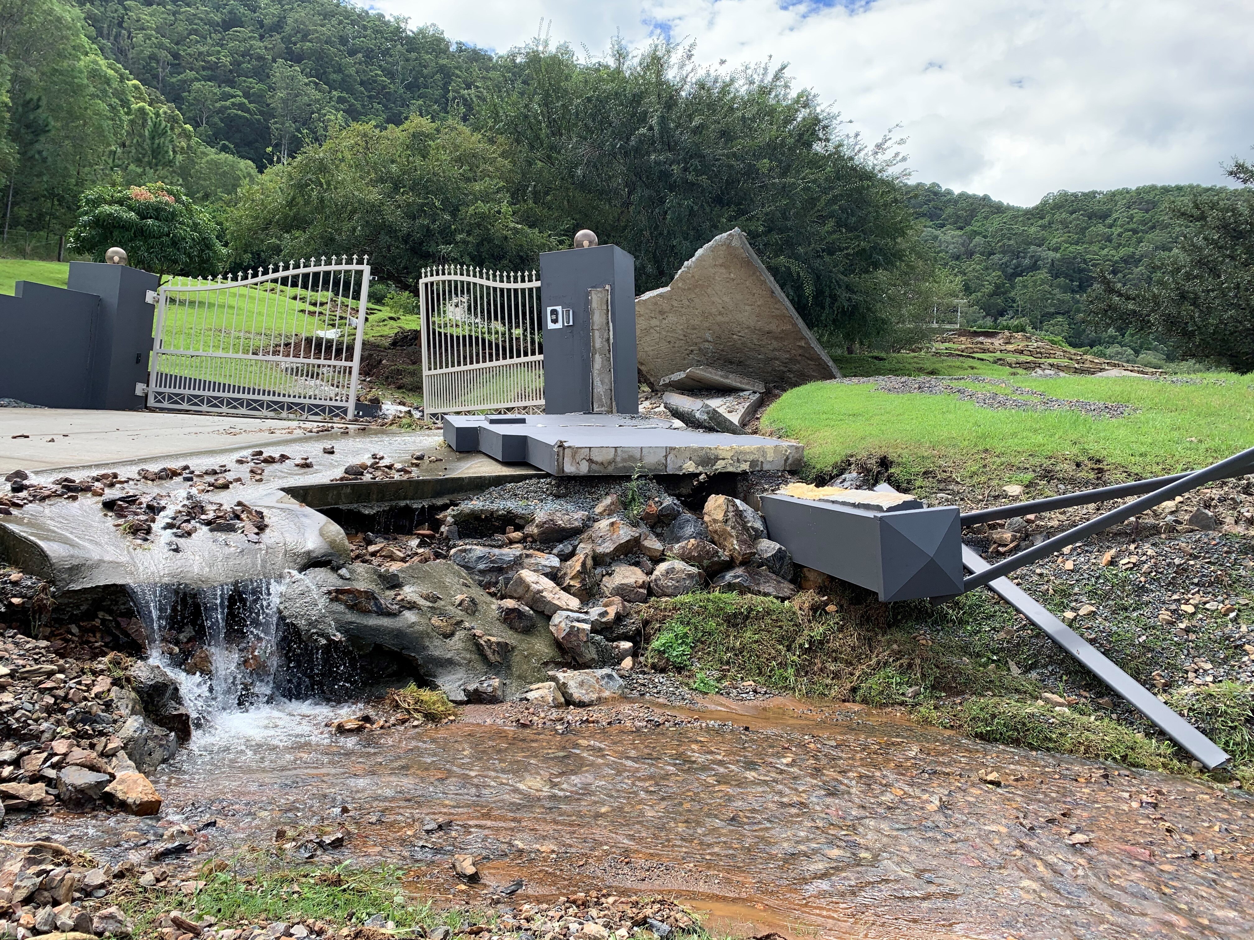 Posts and large slabs of concrete fence skewed along flooded roadway 