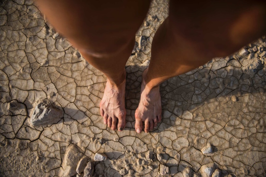 A point of view from above of a woman's feet and legs standing on cracked earth