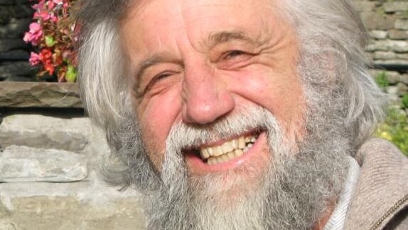 An older man with white hair and a beard holding a rock