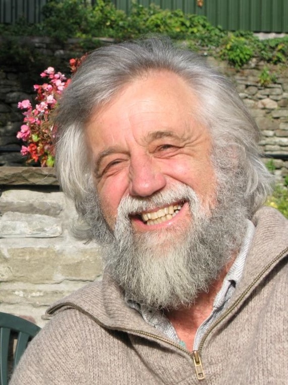 An older man with white hair and a beard holding a rock