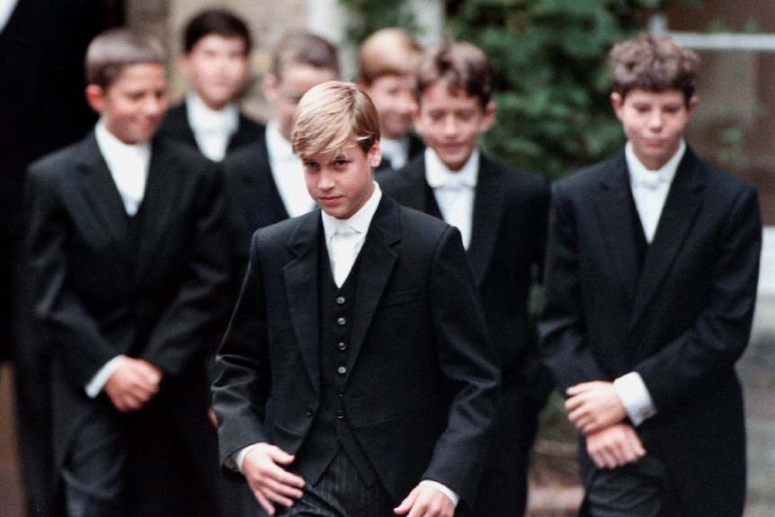 A young Prince William is dressed in Eton College's formal three-breasted suit uniform and walks with classmates.