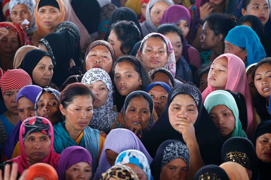 A large group of displaced women look on with concern.