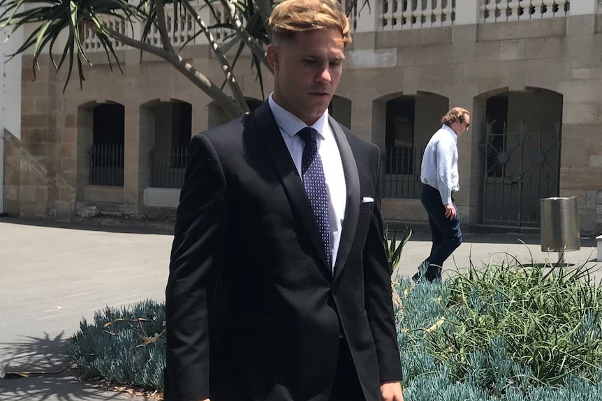 A young man in a dark suit walks through a court complex.