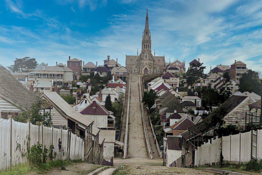 A large church sits at the top of a hill. There are rows of houses along the hill.