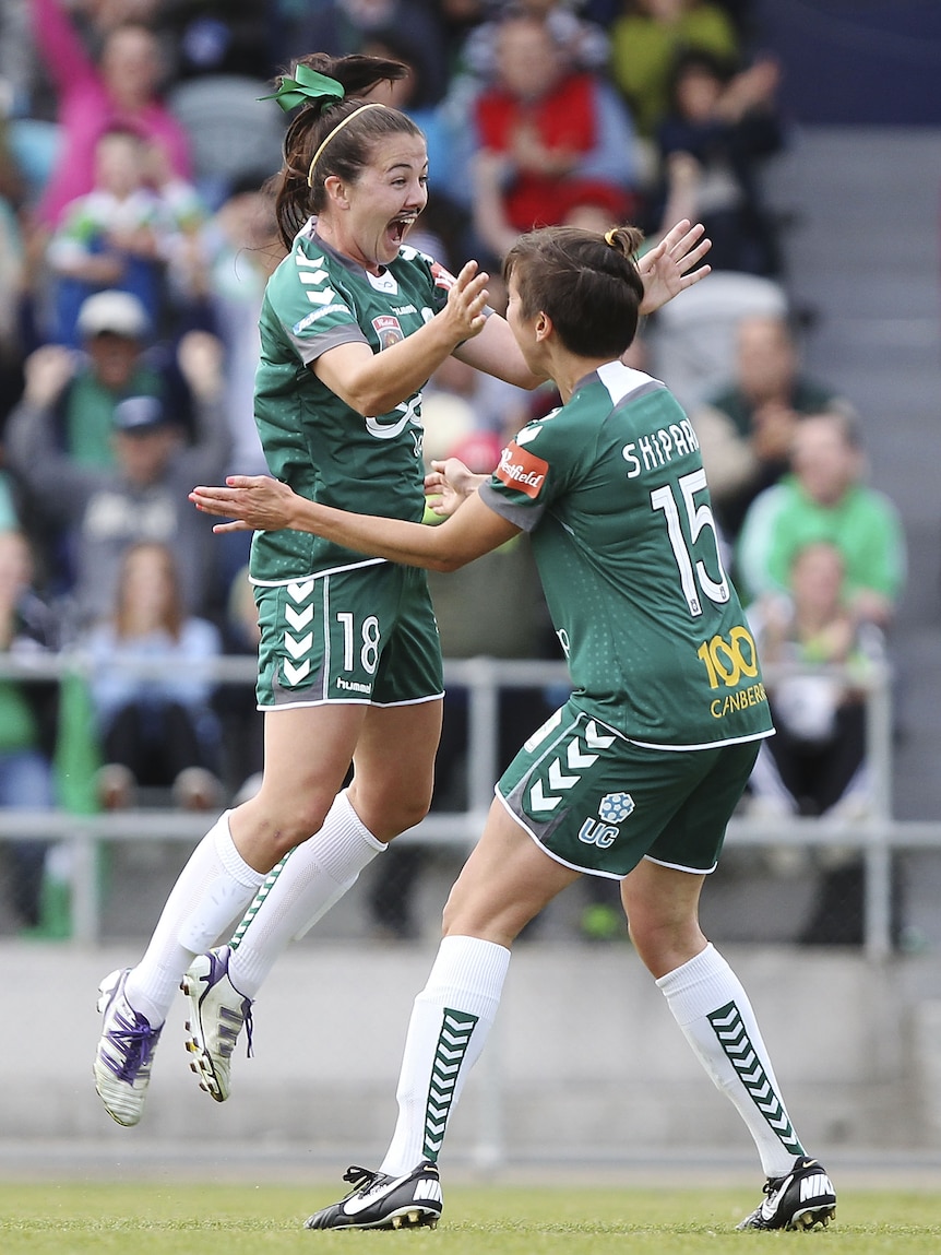 A woman in a soccer kit jumps in excitement into a team-mate's arms