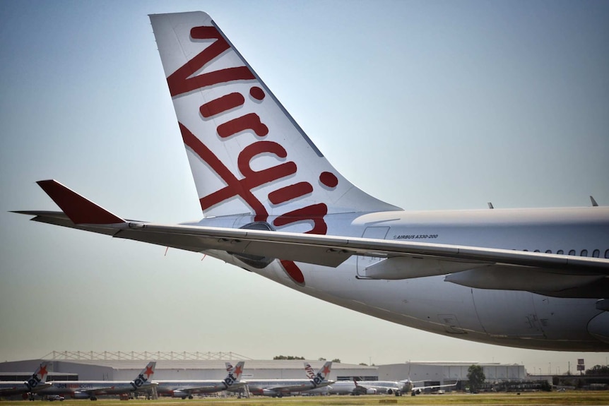 Close-up of tail of a Virgin Australia aircraft with other Jetstar aircraft in distance at Brisbane Airport.