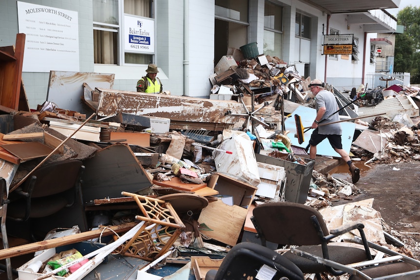 A large pile of rubble pushed up against a building with two people trying to clean it up