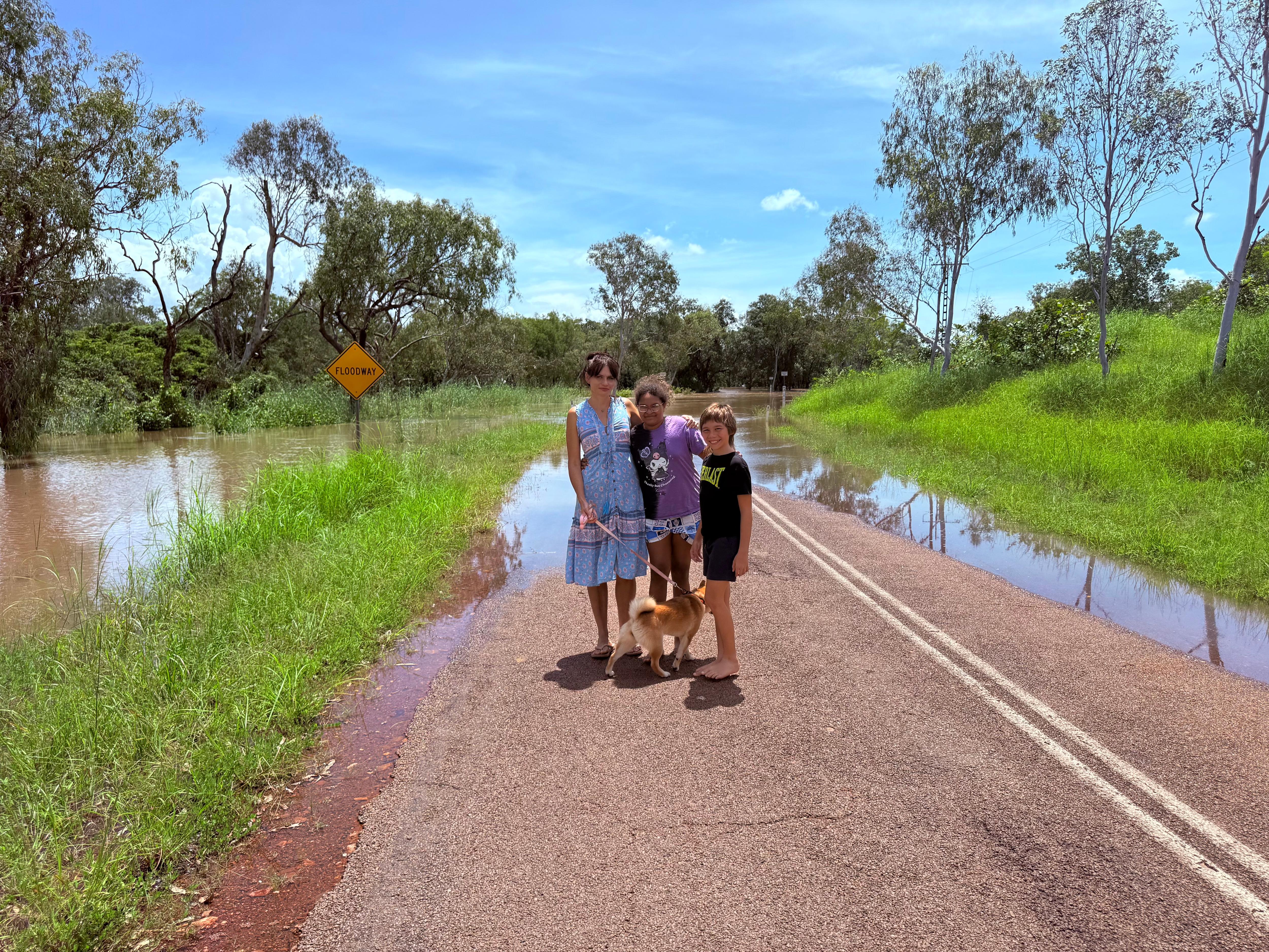 A man, woman and two children with a dog standing in front of a flooded road. 