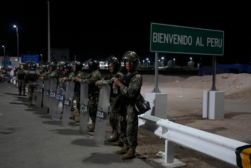An image of Peruvian police with shields lined up next to a sign that says 'Bienvenido al Peru' 