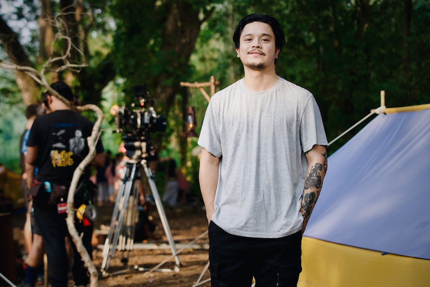 Derby Romero, actor indonesio con camiseta gris, de pie en un bosque.