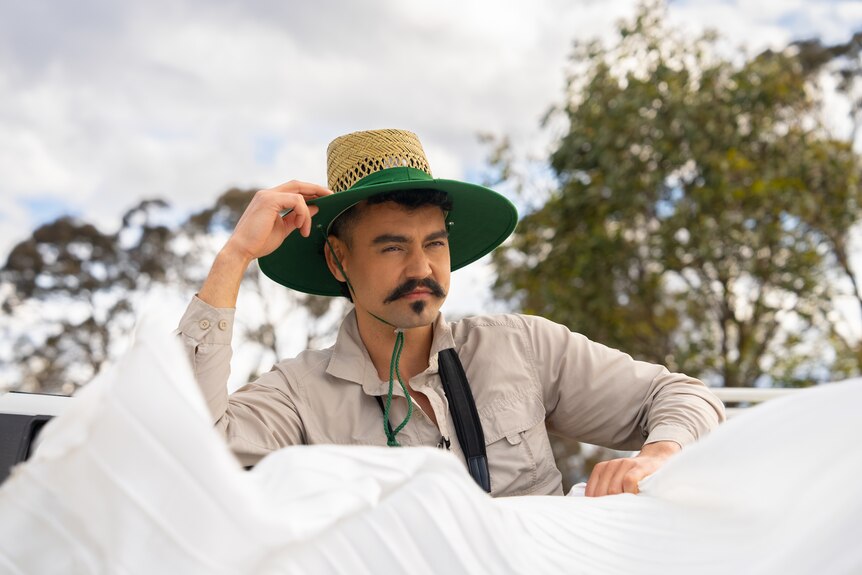 A man in a Bunnings straw hat leans on a white ute.