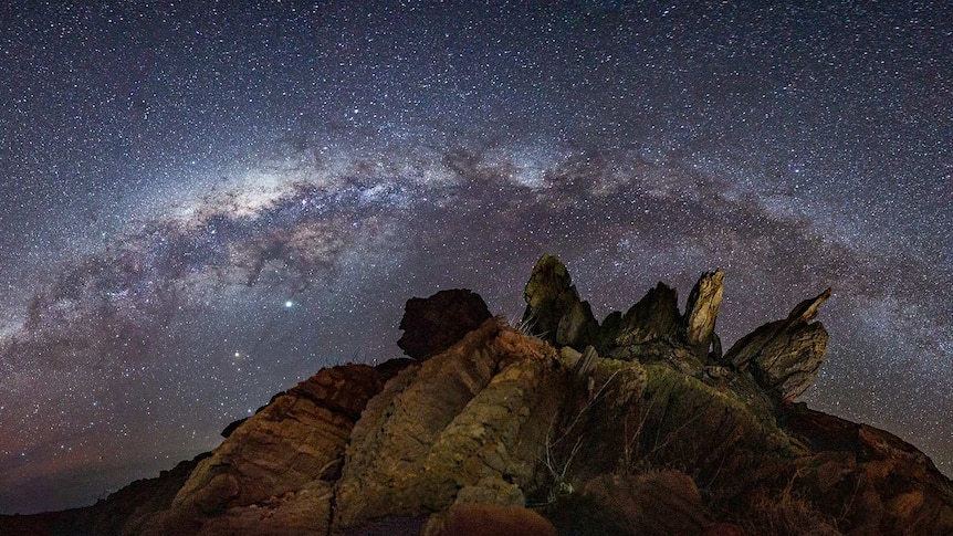 A night sky with rocks in the foreground.