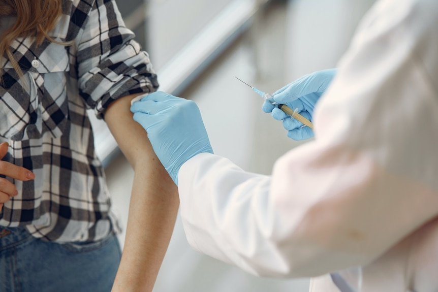 A medical professional in blue gloves prepares to give a woman a vaccine