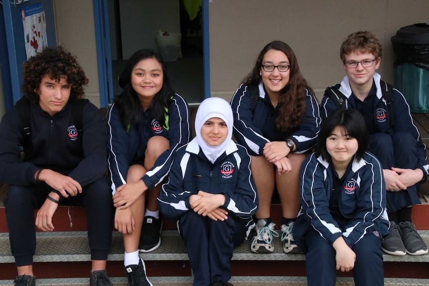 Five students and their older student mentor sit on a step together.