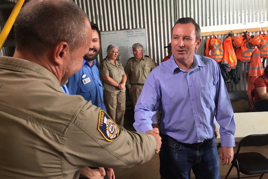 WA Premier Mark McGowan shakes the hand of an emergency services worker as others look on.