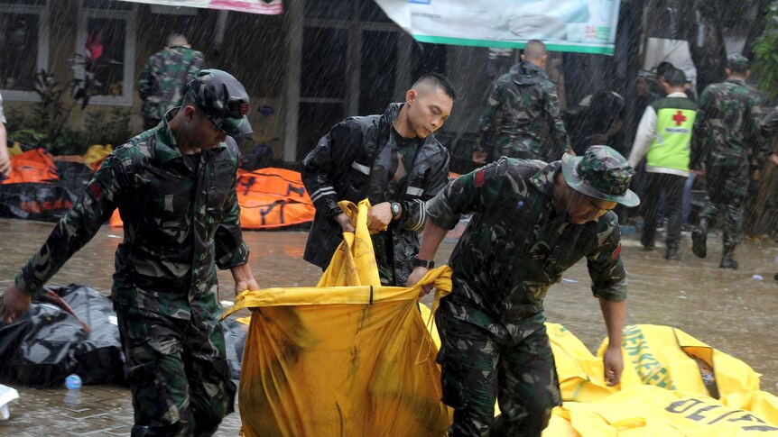 Three soldiers lift a yellow body bag in the rain