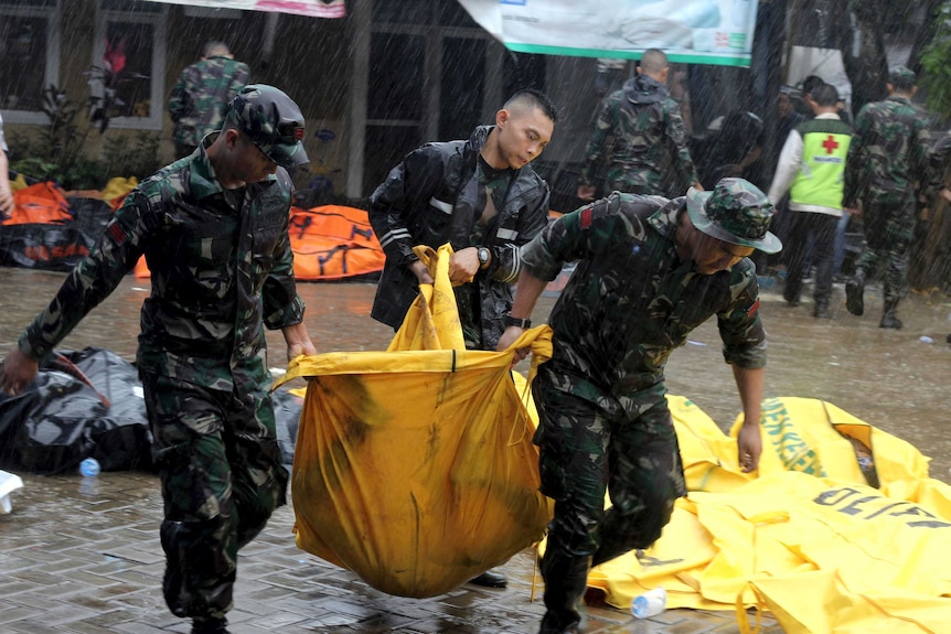 Three soldiers lift a yellow body bag in the rain