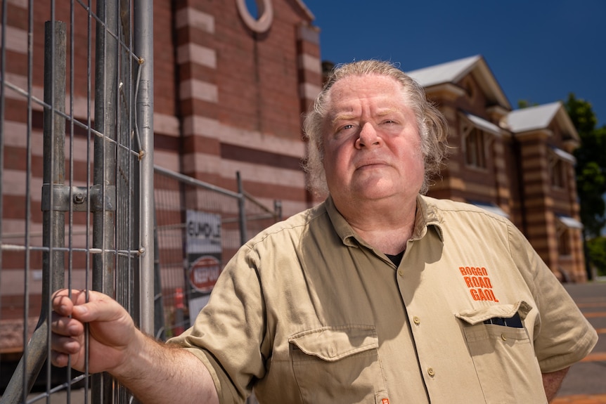 A cross man clutches an iron fence next to a building