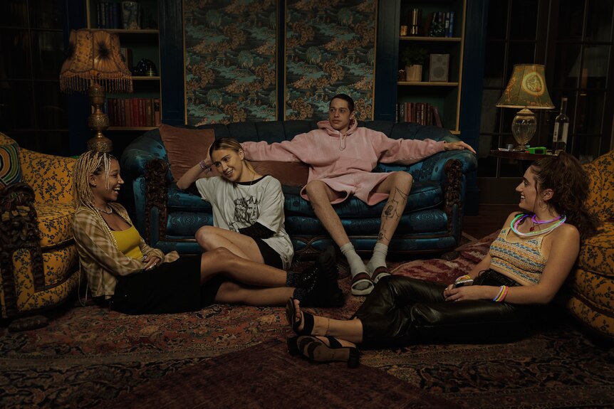 Four people lounge on a couch and on the floor laughing and smiling.