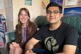 A man and woman sit smiling on a couch.