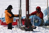 Researchers surrounding by ice focussed on an ice core drill.