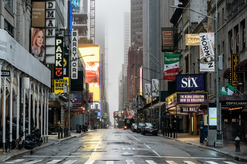 An empty, rain-splattered street with buildings, sign and parked cars on either side