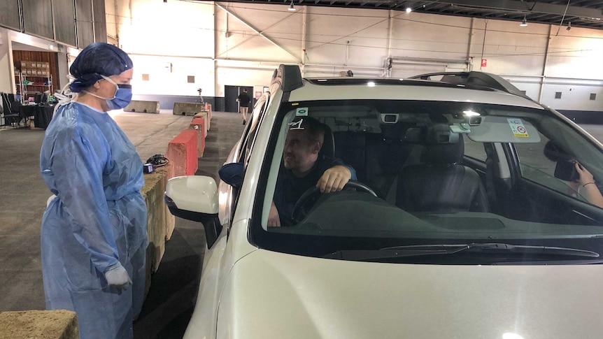 A man in his car leans out his window towards a nurse