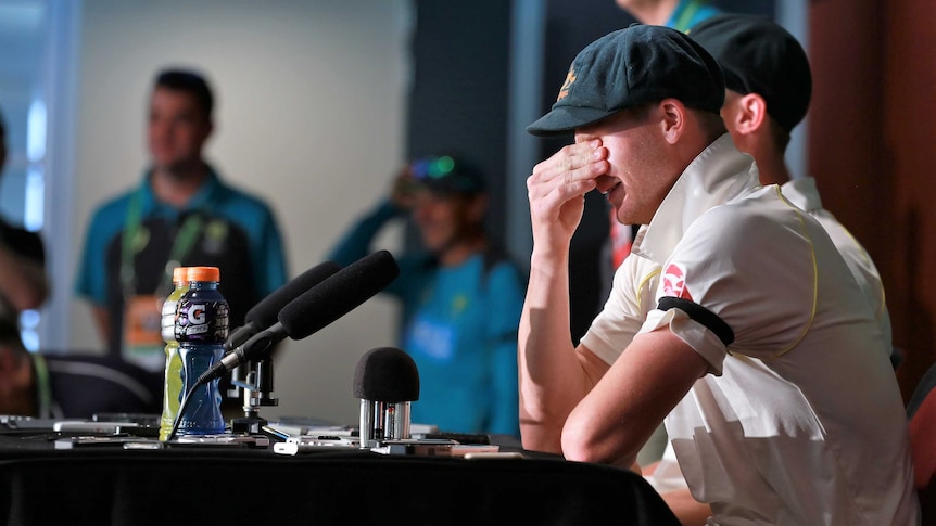 Steve Smith covers his face with his hand as he laughs during a press conference at the Gabba.