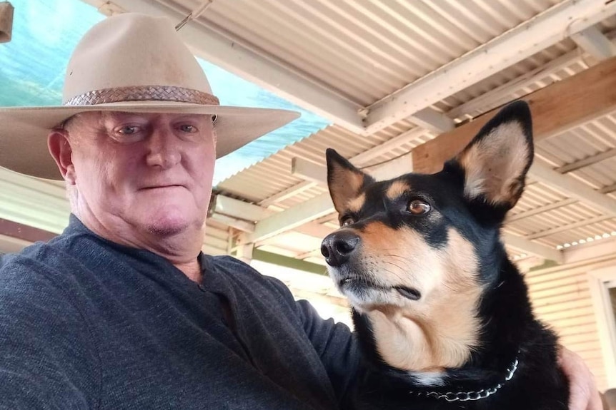 An older man in a blue shirt and brown hat with a black and tan dog looking to the left side
