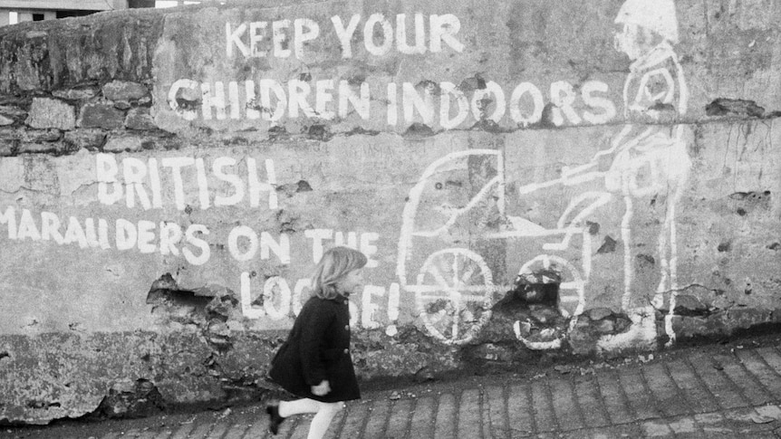Historic photo showing a wall with graffiti: Keep you children indoors. British marauders on the loose. A girl is running past