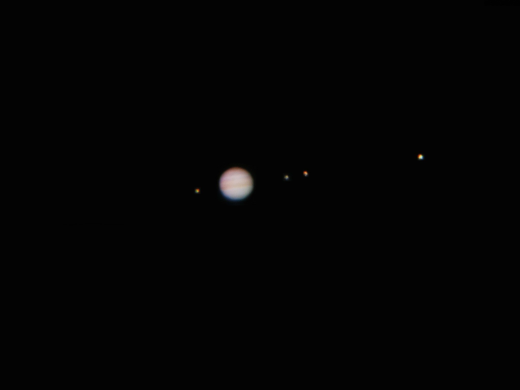 Jupiter is surrounded by four of it's biggest moons which appear as bright spots in the dark sky