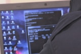 Picture of a person in front of a computer screen filled with code