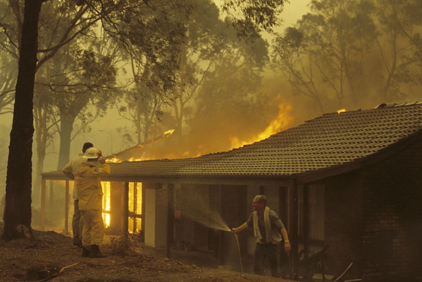 Fire fighters and residents watch a house burn in the 2003 bushfires