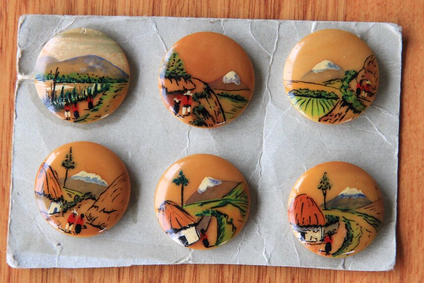 Six buttons featuring African scenes, sitting on a brown table.