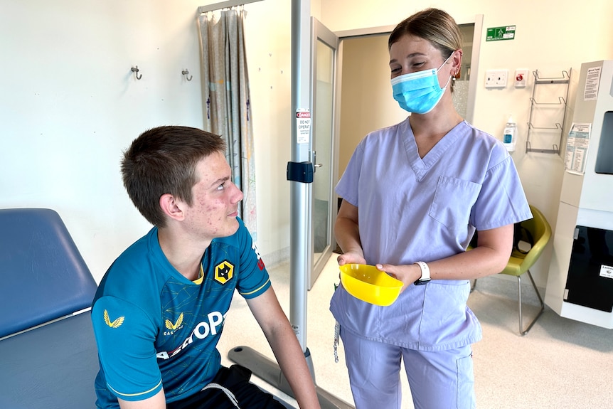 A boy looks up at a nurse with a mask holding a needle.