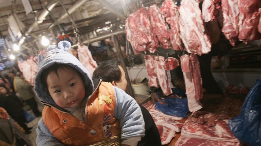A man shouldering a basket with his grandson inside buys meat at a food market in China