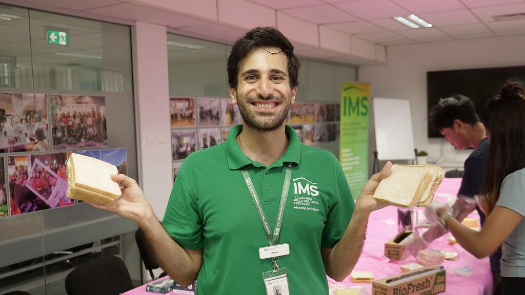A smiling man holding two packets of sandwiches