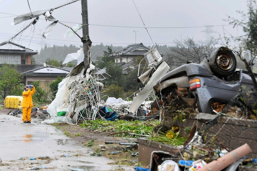 A car is upturned on the side of the road, electricity lines and poles are battered, debris lies everywhere.