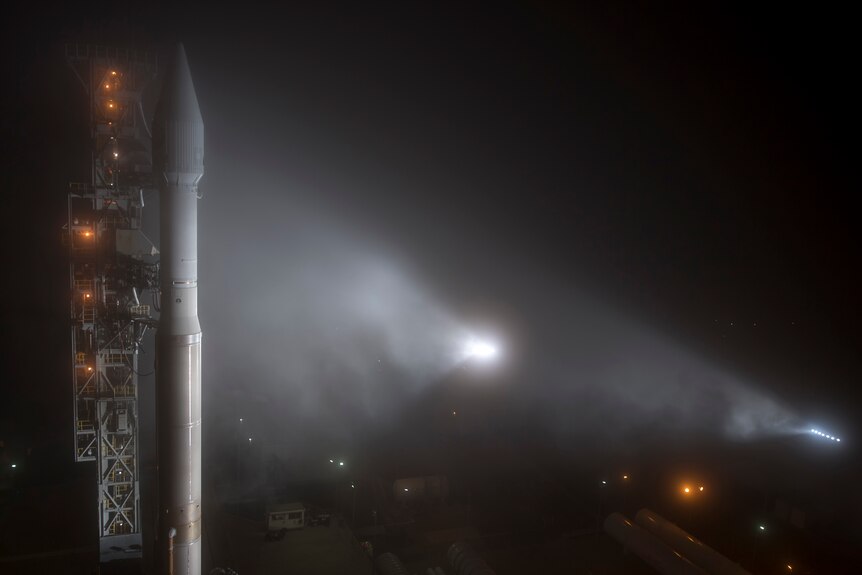 A night-time picture of a rocket sitting on a launch pad in fog.