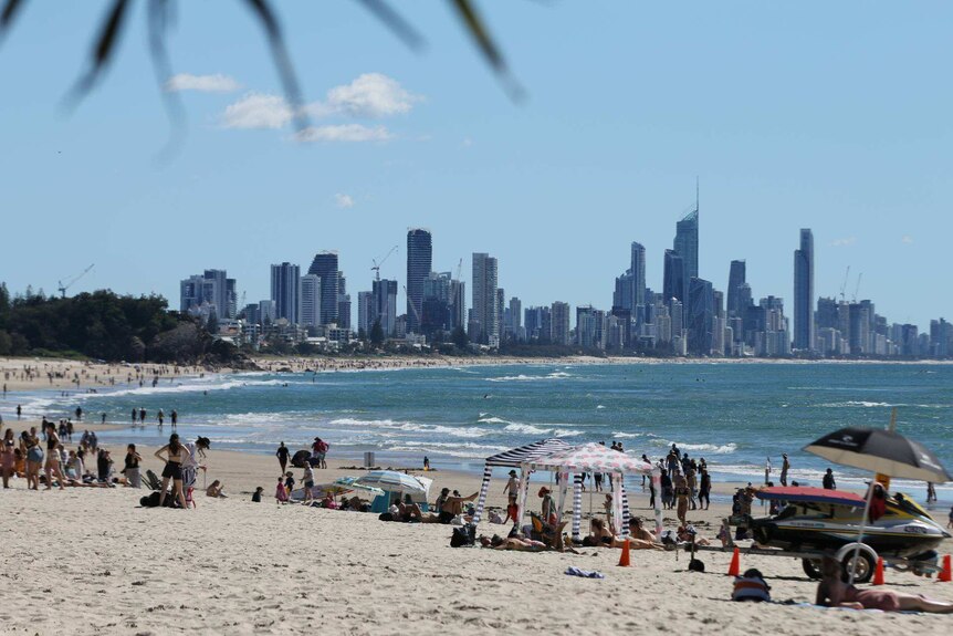 Beach is busy with people and city skyline in background.