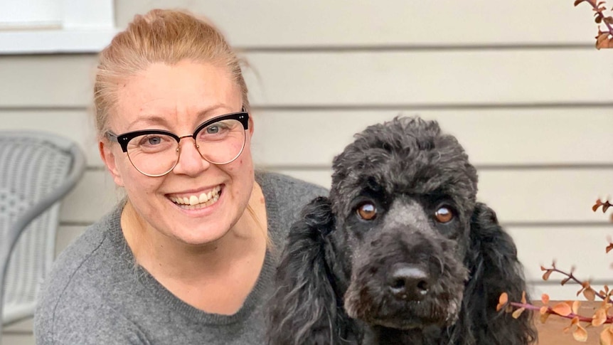 Yolanda Peart-Smith crouching next to her dog, a dark spoodle.