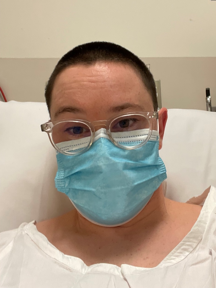 A woman wearing a surgical mask in a hospital bed.