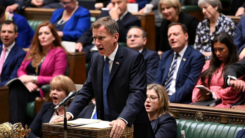 Jeremy Hunt stands at a podium in the House of commons, with other members behind him.