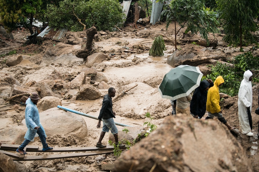 People cross a raging river surrounded by mud in Blantyre, Malawi,