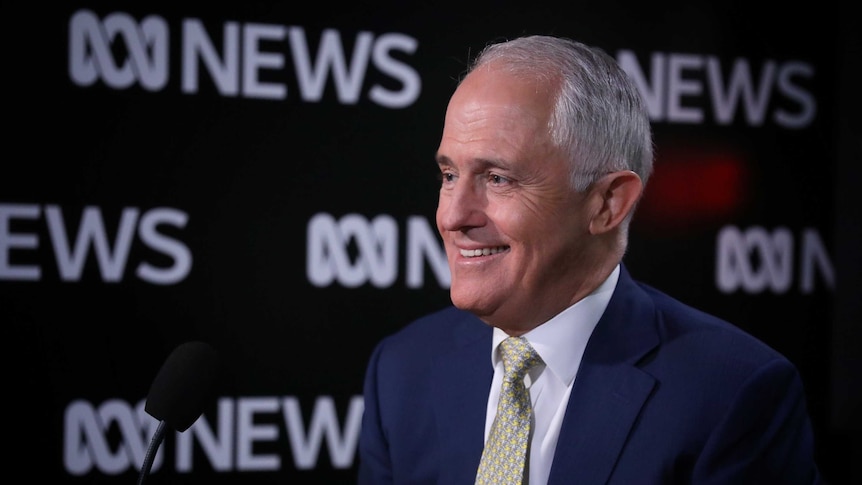 Malcolm Turnbull smiles, looking off camera. Behind him is a wall branded with ABC News logos.